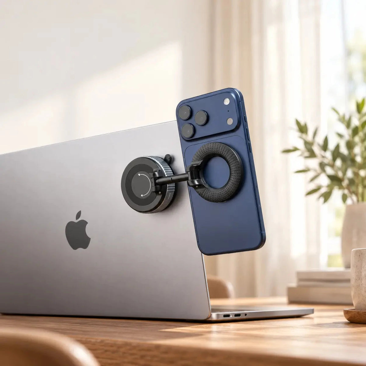 Black magnetic phone holder attaching a blue phone beside a laptop screen.